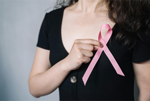 Woman in a black shirt holds a pink bow in her right hand over her left breast